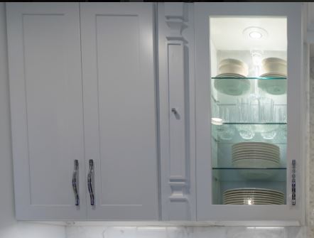 A white kitchen cabinet featuring glass doors, showcasing neatly arranged dishes inside for an elegant display.