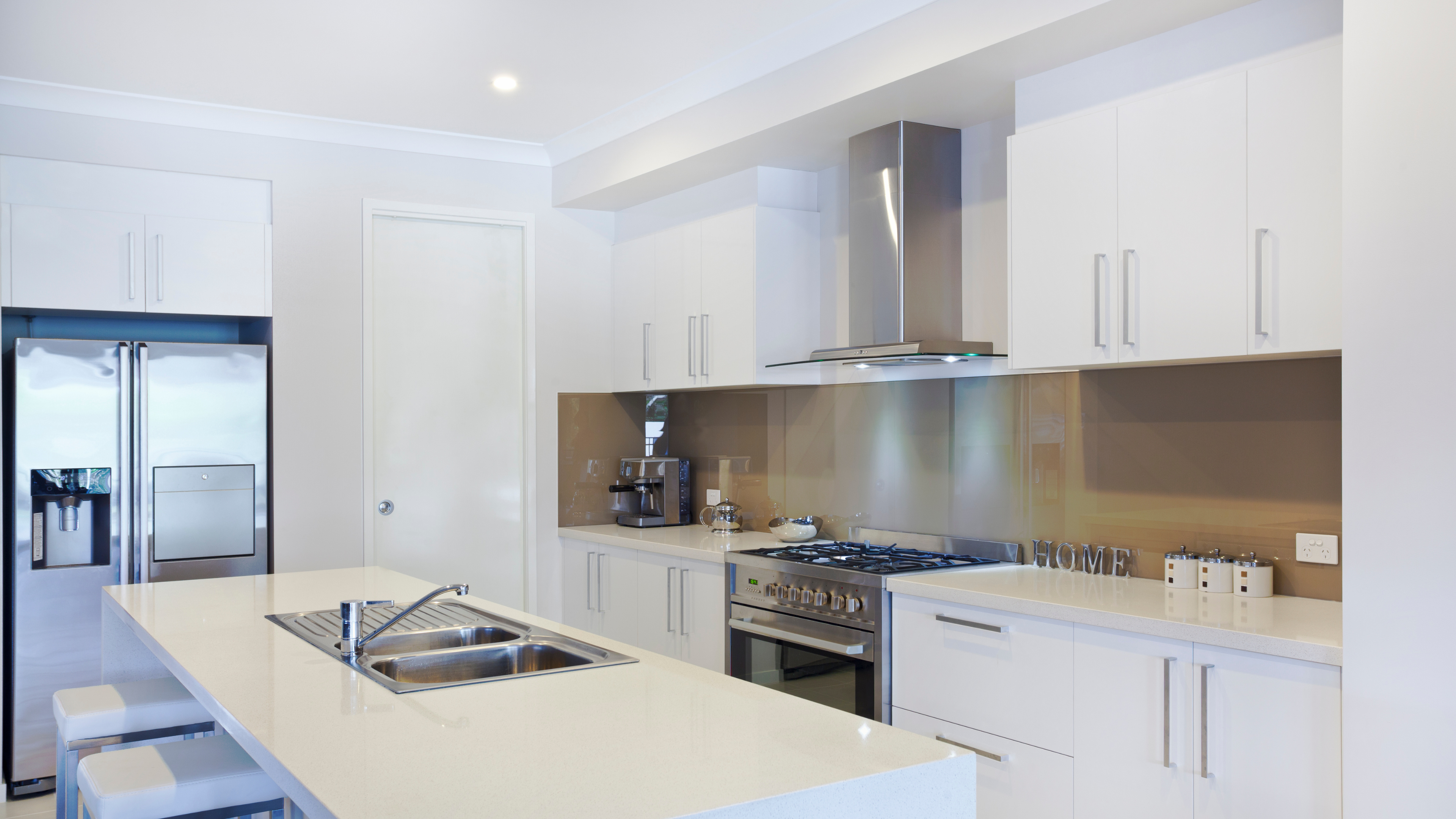 A bright, modern white kitchen featuring sleek cabinets, a spacious countertop, and stainless steel appliances.